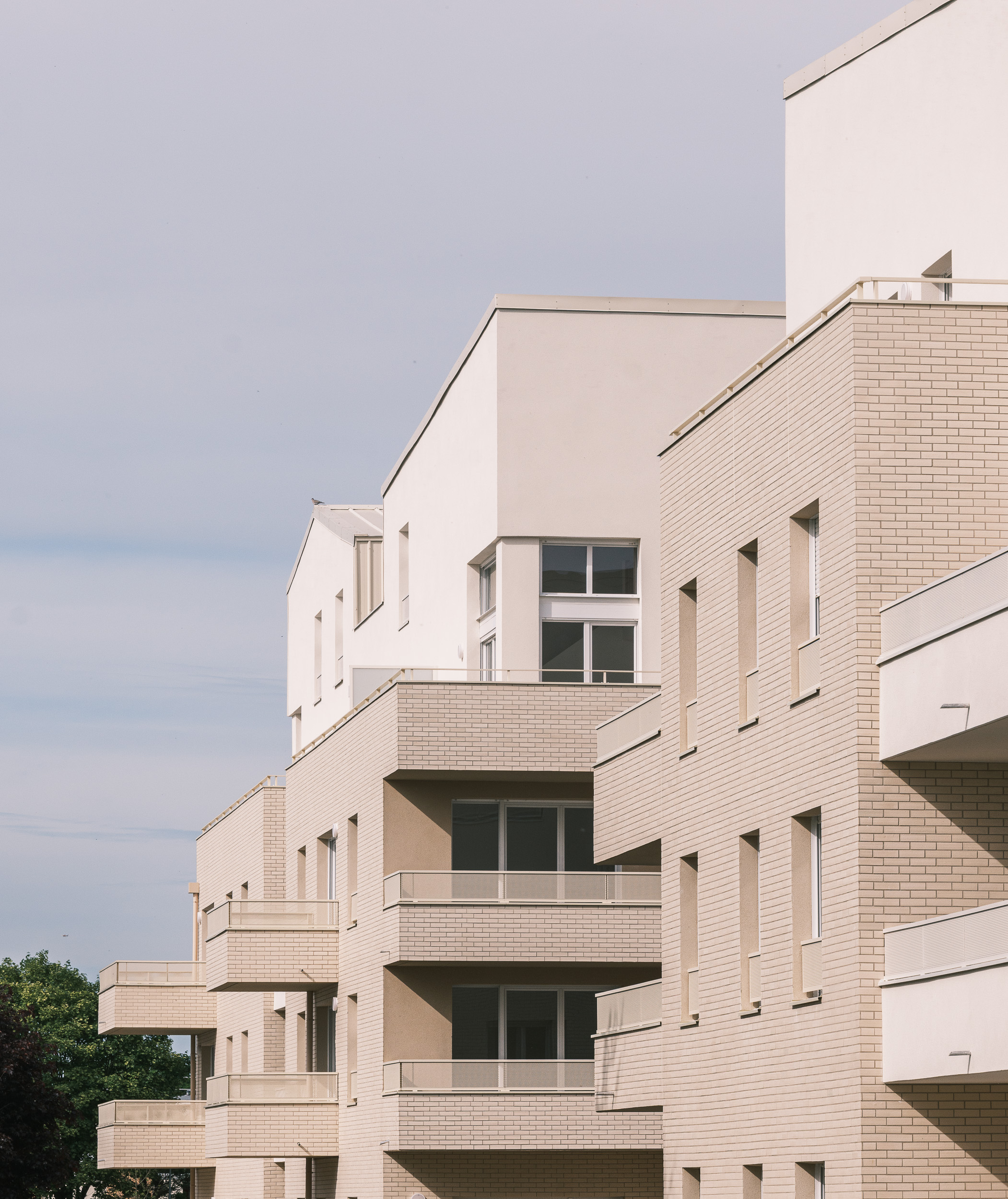 Façades d'une résidence de logements collectifs sociaux aux Clayes-sous-Bois, avec balcons, briques claires, volumes en attique et architecture contemporaine.